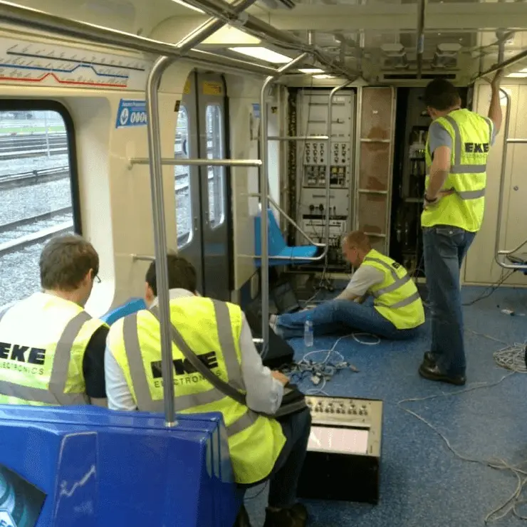 EKE engineers performing testing and commissioning work onboard a train, with diagnostic equipment connected to control systems inside the vehicle.