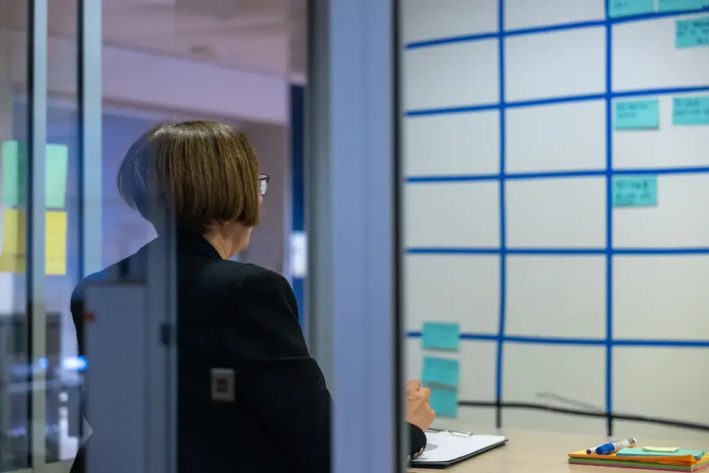 Person reviewing a planning board with notes and schedules in an office meeting space.